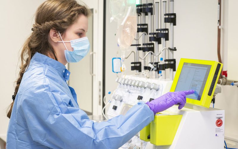 Wetenschapper in beschermende kleding en masker bedient een touchscreen-apparaat in een laboratorium.